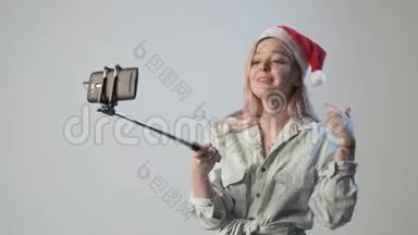 戴着圣诞帽的年轻女孩用智能手机<strong>录制</strong>自拍棒视频